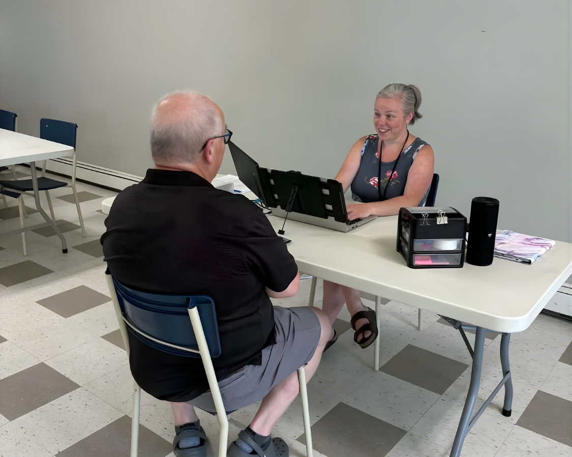 Kasey checks a patient in at a table using a laptop.