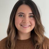 A woman with medium-length dark blonde hair wears a red shirt and is smiling at the camera.