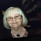 Photo of a woman with chin-length white hair, glasses, and she's smiling into the camera. 