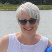 A woman wearing sunglasses is smiling in an outdoor setting.