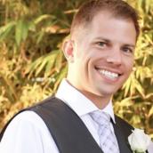 A man with short, blonde hair is wearing a vest, dress, shirt and tie is smiling at the camera.