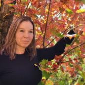 Woman with brown hair and a black shirt is outdoors beneath a tree.