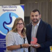 Dr. Ahmed Jad presents an award to Alana Toole, Perioperative Services Director, Northern Zone, in recognition of her commitment to advancing obesity care and improving patient accessibility. They are standing side by side, holding the award, smiling toward the camera.