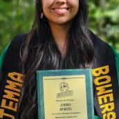 Outdoors with trees in the background, a smiling woman holds a certificate.