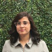 In a portrait capture, a woman is smiling while wearing glasses in an outdoor setting.