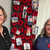 Two smiling women are standing in front of an indoor display filled with vibrant colours and images. 