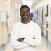 A photo of a man holding a white x-ray machine. He has brown hair and facial hair. He is wearing a white sweater with grey pants. 