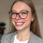 A woman wearing glasses is smiling while in an indoor setting.