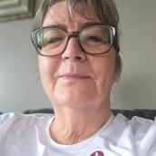A close-up of a woman wearing glasses with a calm and gentle expression dressed in a white shirt with the logo and name "St. Mary’s Memorial Hospital" printed on it.