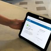 A hand holds a tablet showing the Virtual Urgent Care login screen.