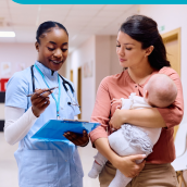 Woman stands wearing scrubs and a stethoscope beside a woman holding an infant baby.