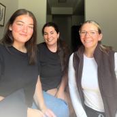 Three smiling women are seated closely together indoors. 