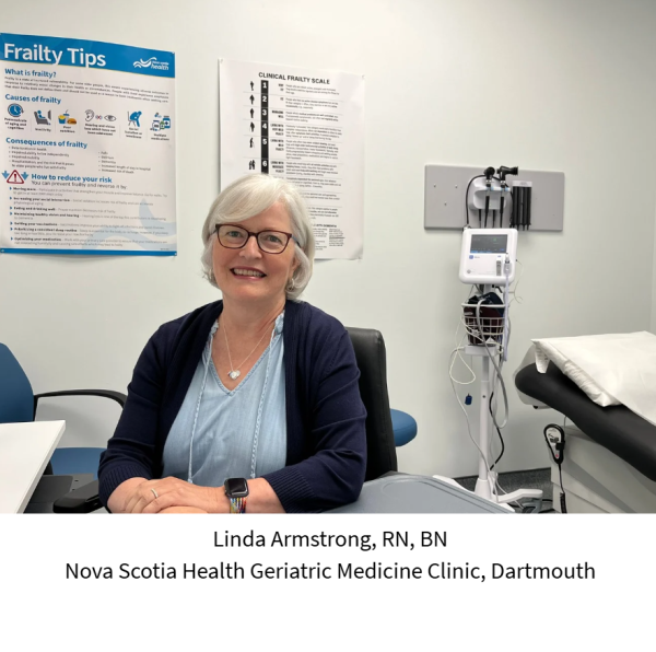 A woman with short, white hair and glasses wears a navy sweater over a light-blue v-neck shirt and she's sitting in a doctor's office with medical equipment in the background, smiling at the camera.