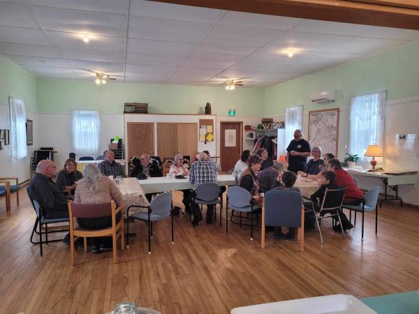 A group of people is gathered around a table in an indoor setting. The atmosphere suggests a living or dining room environment. 