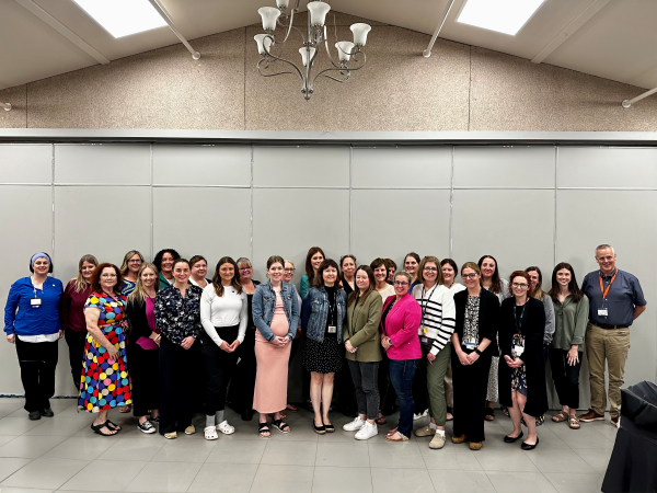 A group of about 25 people stand together in a large room, smiling at the camera. They are dressed in a mix of professional and casual clothing, with some wearing Nova Scotia Health badges. The group represents Aberdeen Hospital leaders who took part in the new safety education pilot.