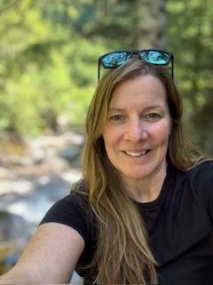 Woman with long, blonde hair is wearing a black t-shirt and sunglasses on her head and is smiling at the camera.