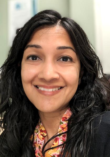 A woman is smiling for the camera. She has a joyful expression. The portrait captures her indoors; a typical look consistent with portrait photography. 