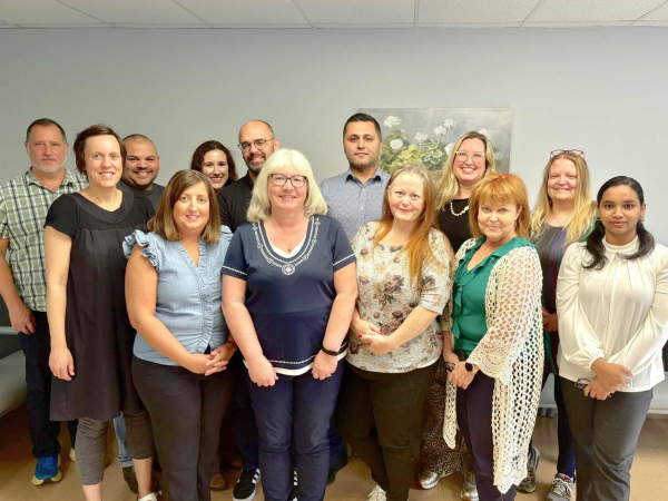 A group of 13 people in casual business attire stand together and smile at the camera.