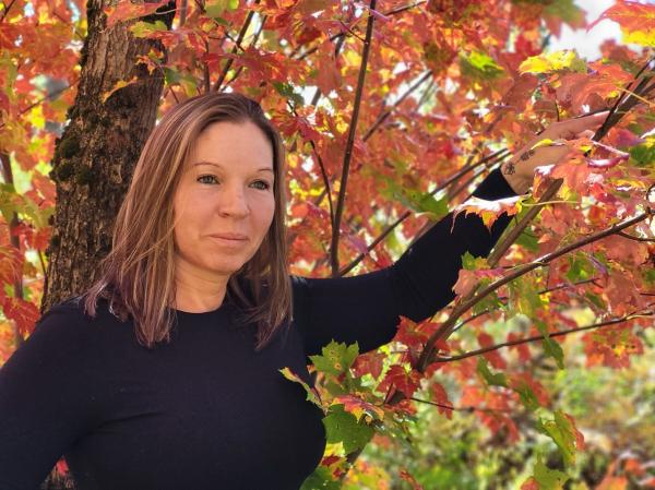 Woman with brown hair and a black shirt is outdoors beneath a tree.