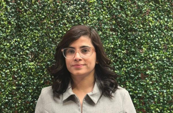 In a portrait capture, a woman is smiling while wearing glasses in an outdoor setting.