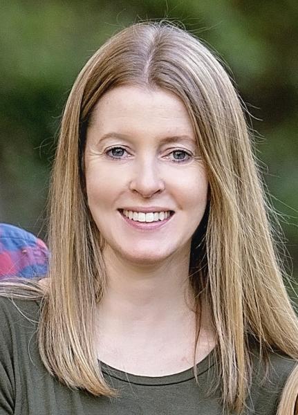 A woman with long, blonde hair stands outdoors and is wearing a green shirt.