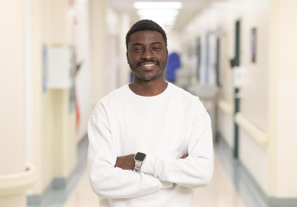 A photo of a man holding a white x-ray machine. He has brown hair and facial hair. He is wearing a white sweater with grey pants. 