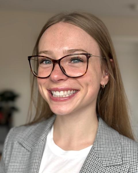 A woman wearing glasses is smiling while in an indoor setting.
