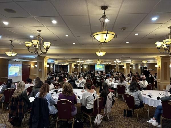 Groups of people sit at tables in a large conference room.
