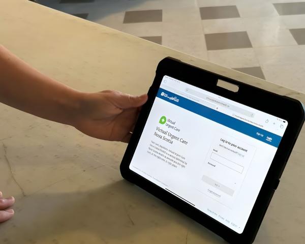 A hand holds a tablet showing the Virtual Urgent Care login screen.