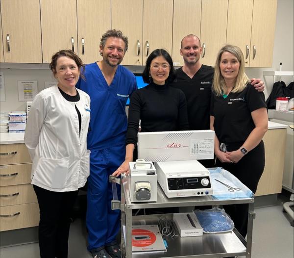 Five people stand together in front of a piece of hospital equipment smiling at the camera.