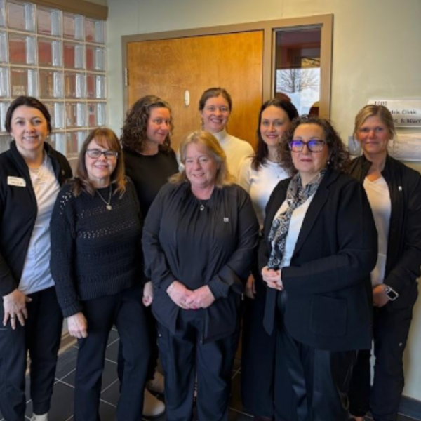 8 medical staff gathered for a group photo. There is a brown door behind them and a glass wall with little squares.