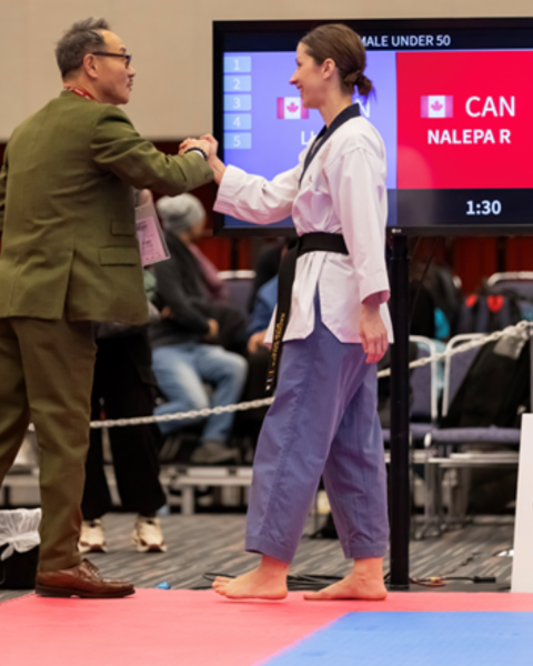 Photo of a woman in taekwondo uniform shaking a man's hand in a green suit.