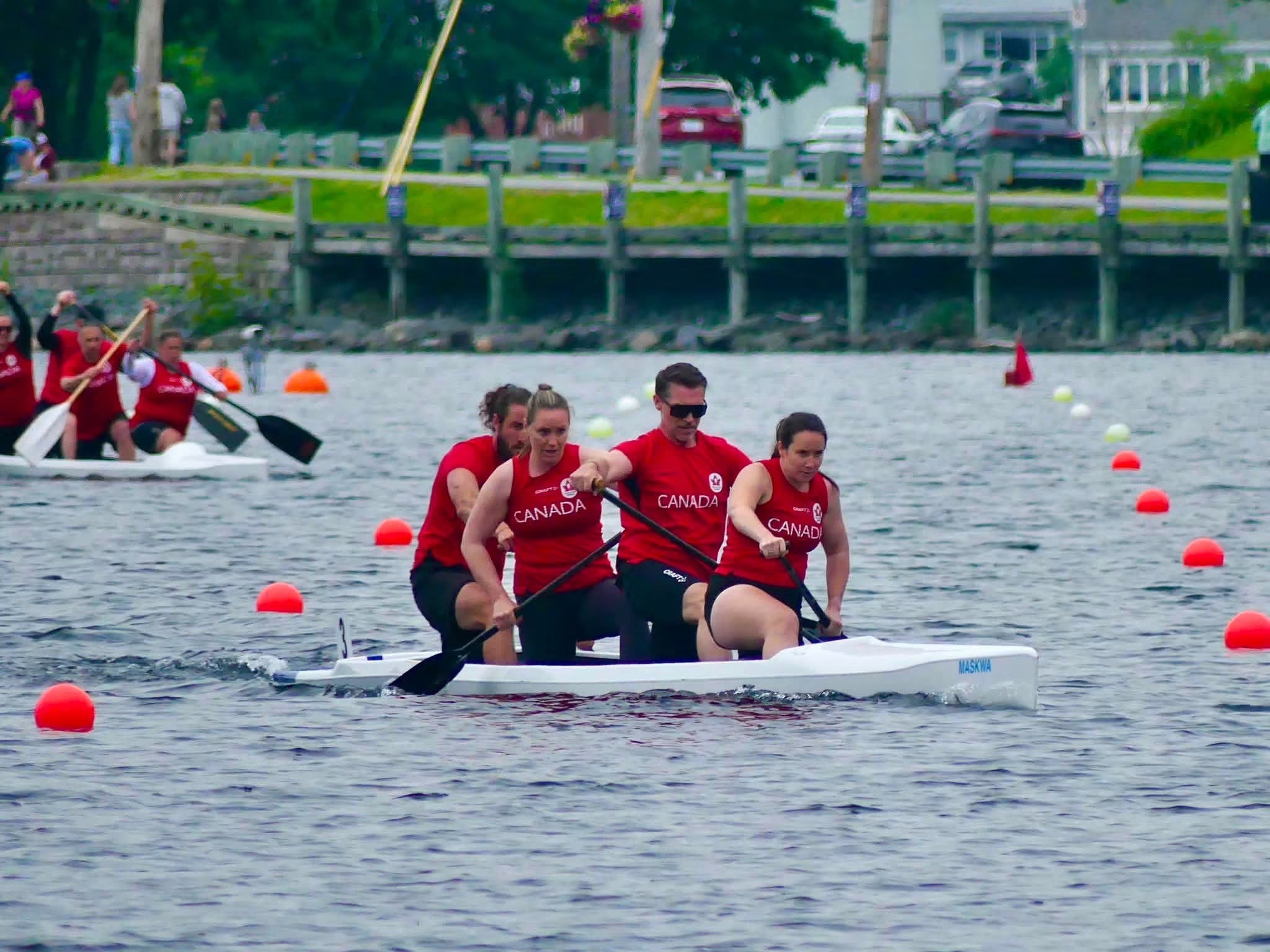 Four people in a kayak wearing red Canada shirts paddle on the water.