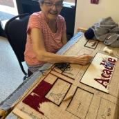 A woman is sitting at a table and the setting includes a rug on the floor. 