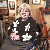A woman sits in a wheelchair, smiling for the camera.