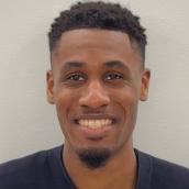 Headshot of a man wearing a black shirt and name badge is smiling at the camera.