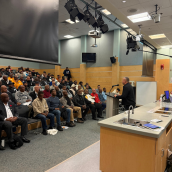 A photo of a conference for the black community. Attendees are seated and there is a speaker in front of the podium.