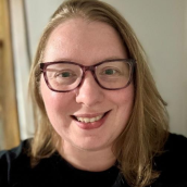 Picture of a woman with shoulder length hair smiling largely wearing glasses. 