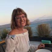 Picture of a woman with shoulder length hair and glasses pictured outside with a beautiful view smiling.