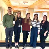 A group of five people stand together inside a health care facility smiling at the camera.