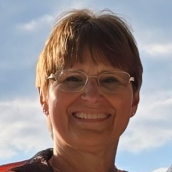 Image of a woman with short light brown hair, wearing glasses and smiling largely outside.