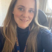 A headshot of a woman with long light brown hair smiling, wearing an NSGEU lanyard.