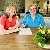 Two women sitting at a table with a paper in front of them. 