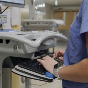 Image of a healthcare worker typing on a keyboard. The healthcare is standing using a WOW (workstation on wheels).