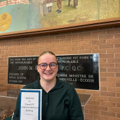 Image of a person wearing glasses holding a certificate in their hand.