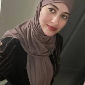 A woman with brown eyes wears is taking a selfie wearing a light brown headscarf and dark brown shirt.
