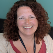 Close up image of a woman with shoulder length dark curly hair and she is smiling. 