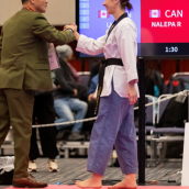 Photo of a woman in taekwondo uniform shaking a man's hand in a green suit.