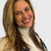Picture of a woman with long light hair smiling wearing a white turtleneck and a stethoscope around her neck.