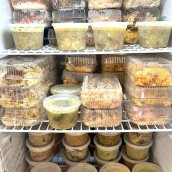 The inside of a cooling display, packed tightly with neatly stored food containers on wire shelves. 